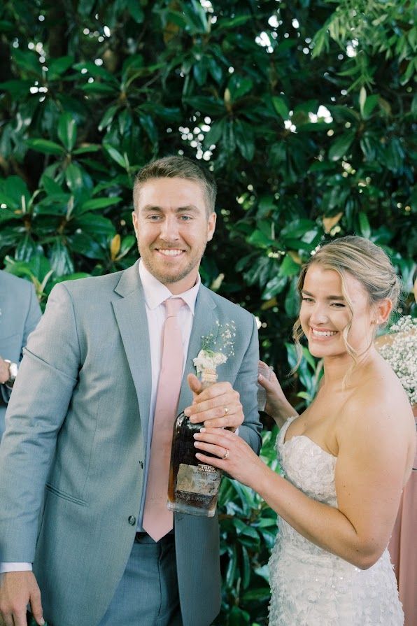 A bride and groom are standing next to each other holding a bottle of wine.