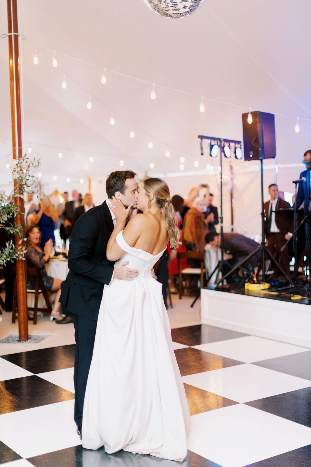 A bride and groom are kissing on a checkered dance floor at their wedding reception.