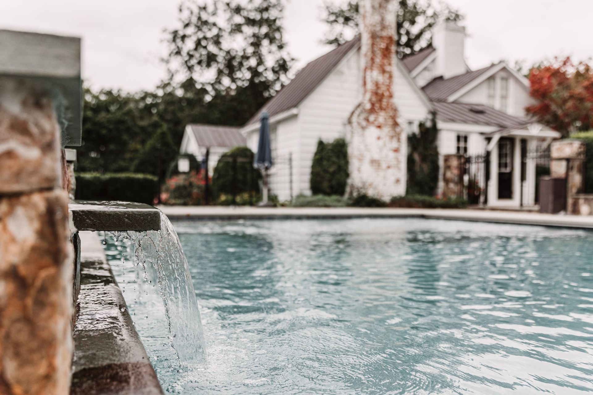 A swimming pool with a waterfall and a house in the background.