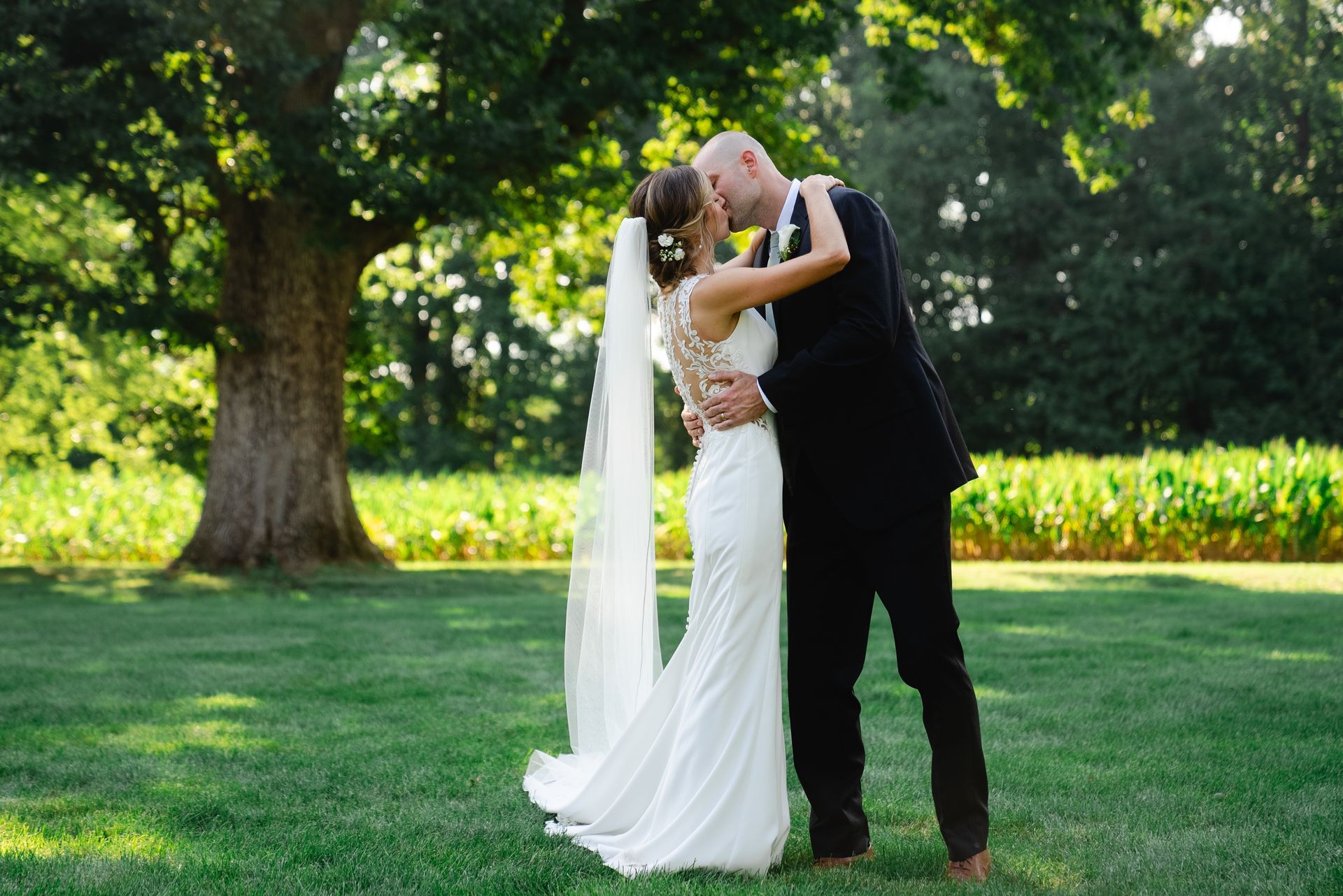 A bride and groom are kissing in a grassy field.