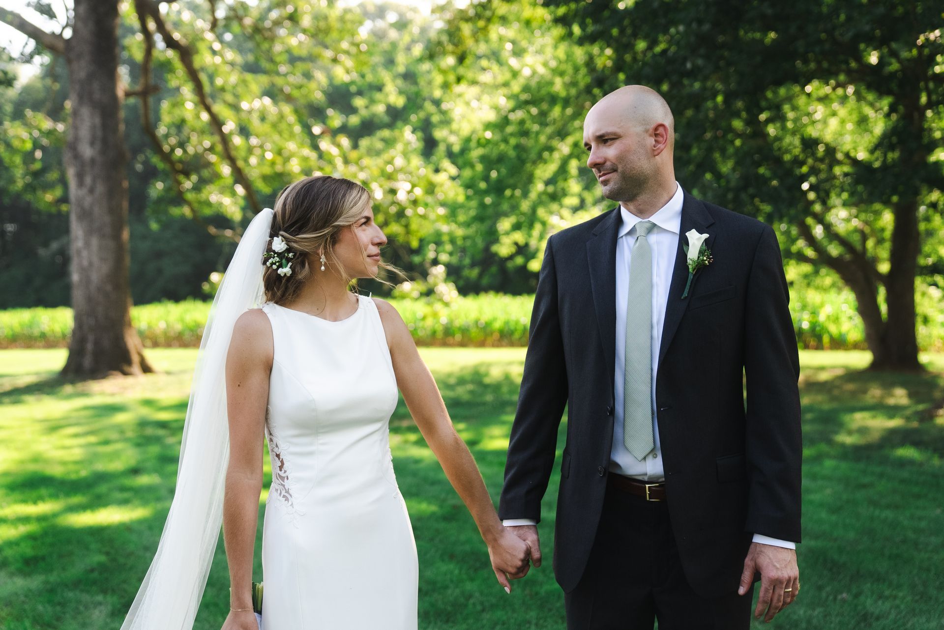 A bride and groom are holding hands and looking at each other in a field.