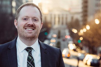 Man in suit smiling in front of a city street and building.