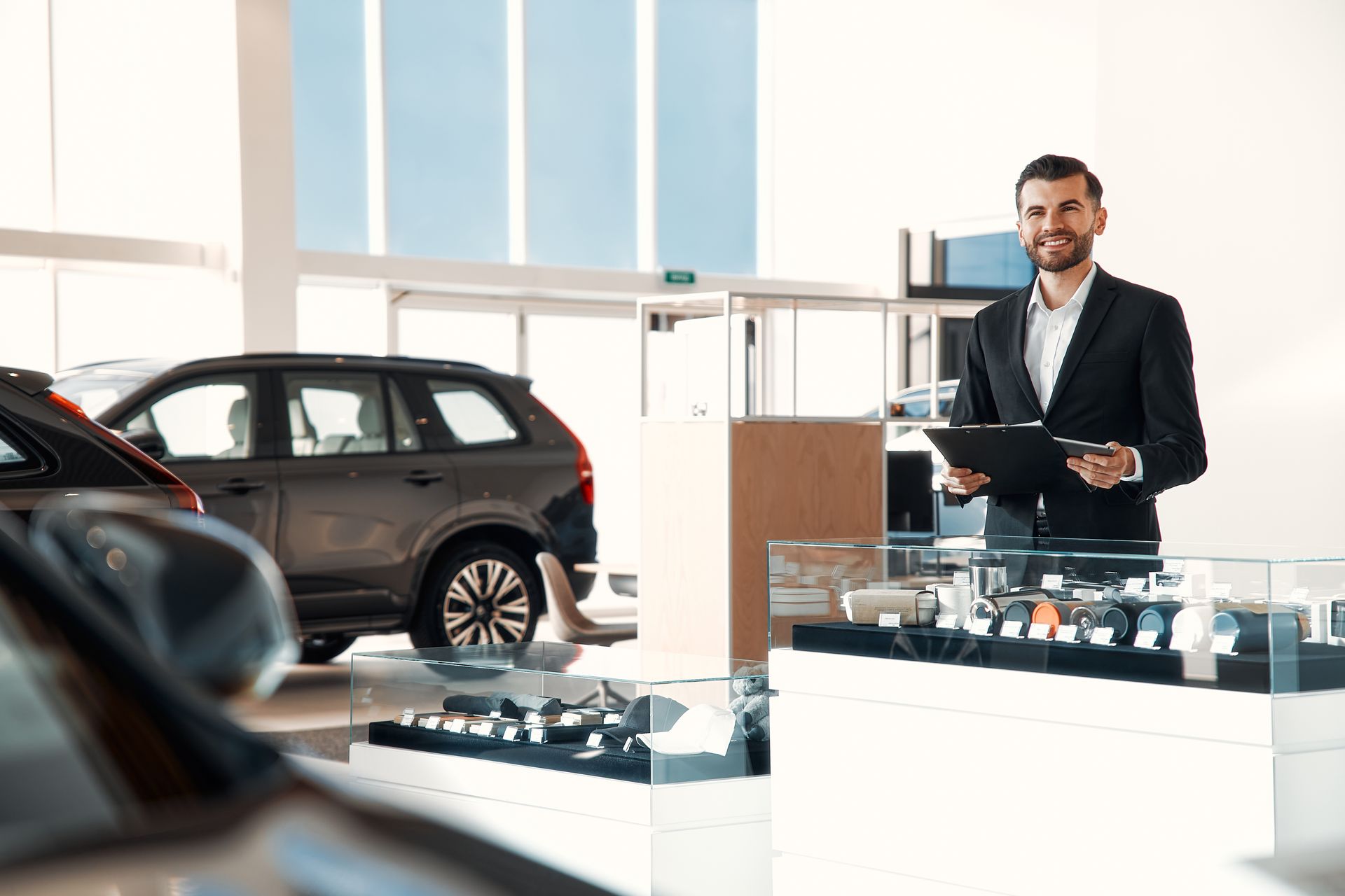 A man is standing in a car showroom holding a clipboard.