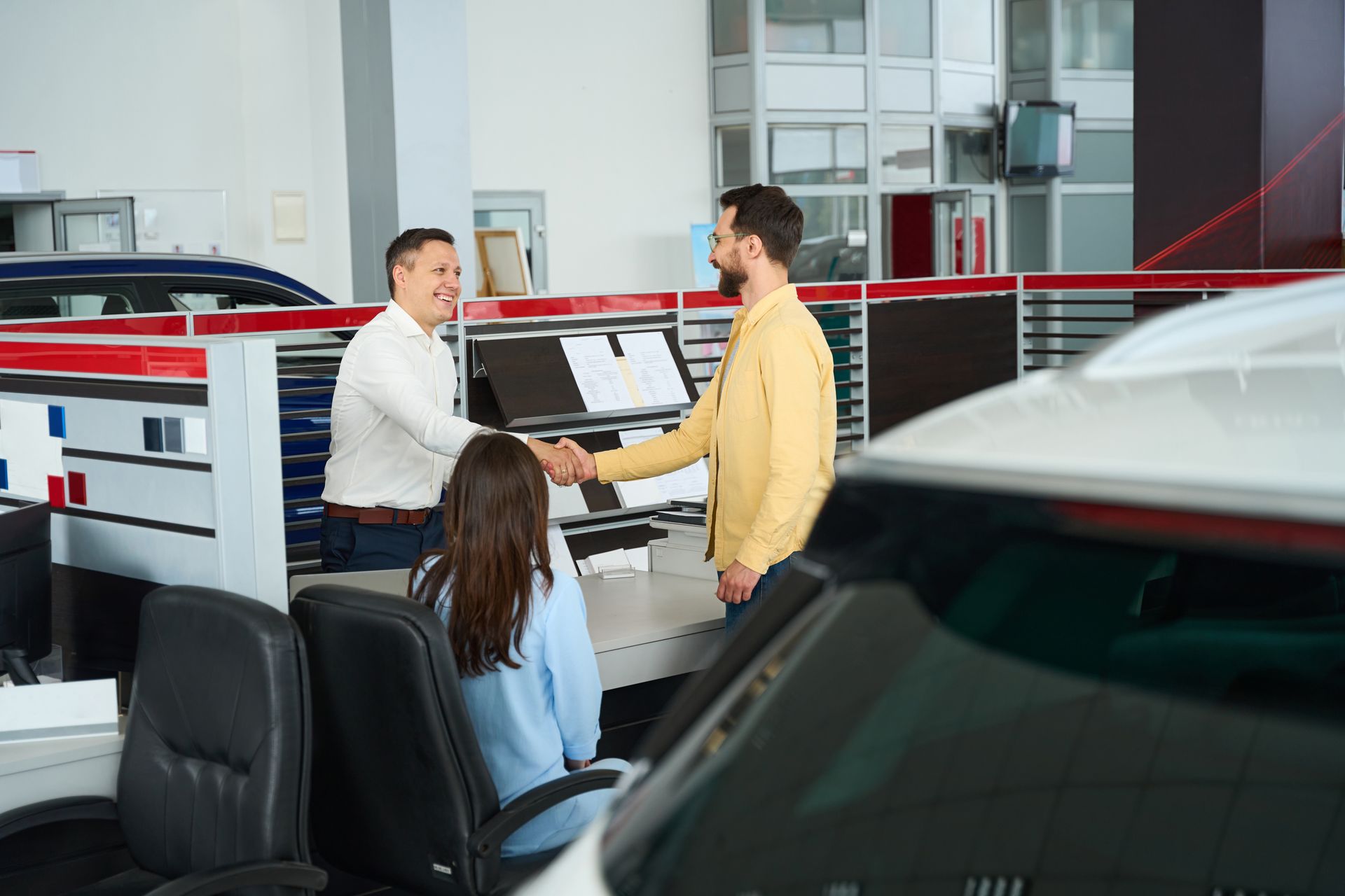 A man is shaking hands with a woman in a car showroom.