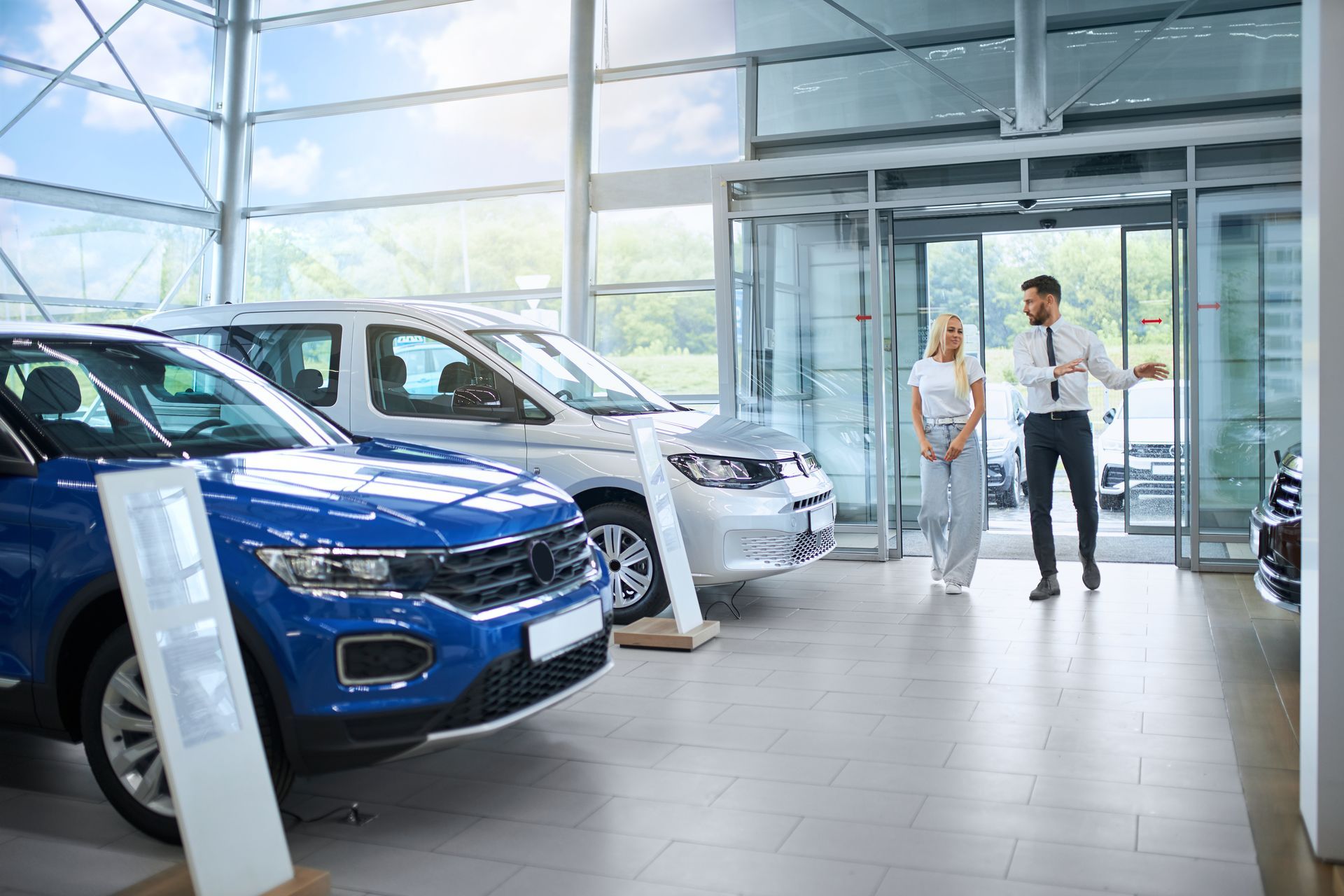 A man and a woman are standing in a car showroom looking at cars.