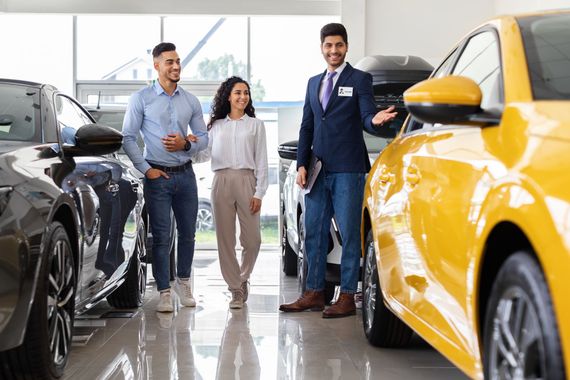 A group of people are standing in a car showroom looking at cars.