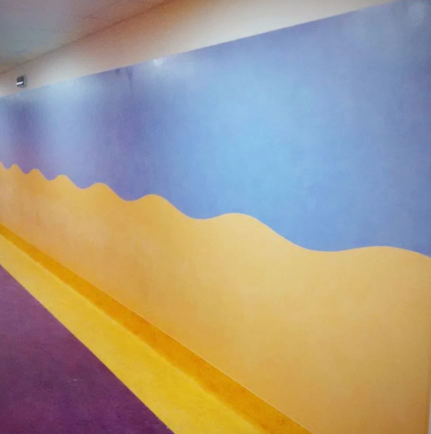 Parete dipinta di colori vivaci con motivi ondulati gialli e blu.