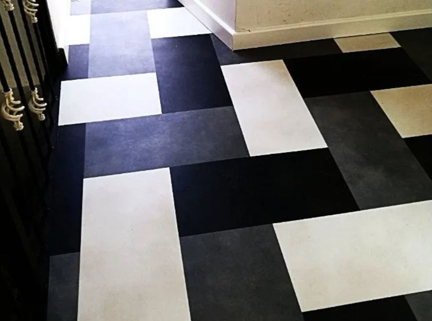 Piastrelle geometriche nere, bianche e grigie sul pavimento di un corridoio.