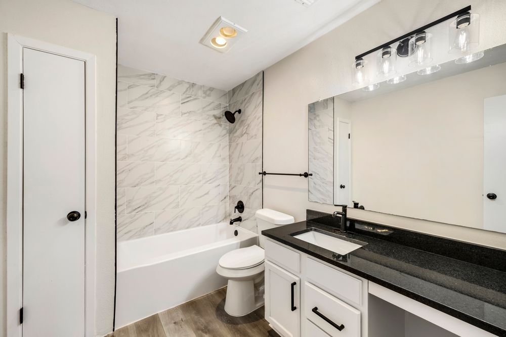 Bathroom with white cabinetry, black countertop, marble-look shower surround, and a rectangular mirror.
