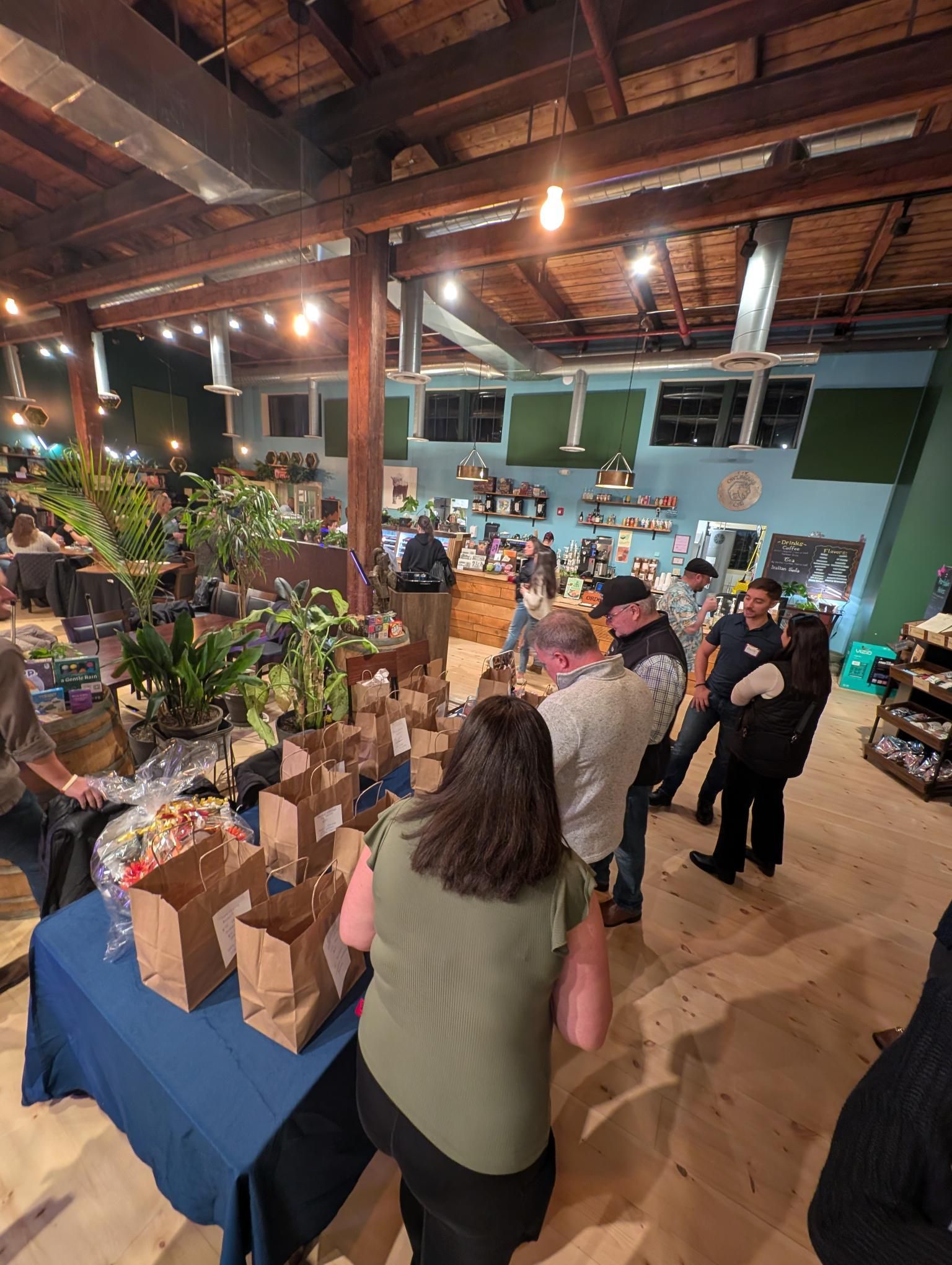People at an event with food bags on a table, inside a building with plants and a counter.