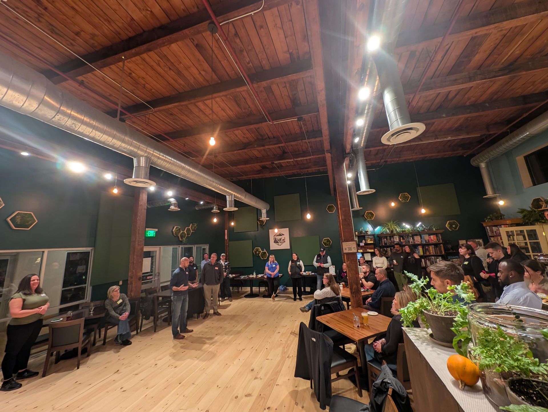 People at an event in a room with wood floors and ceilings. Speakers are in front of a crowd.