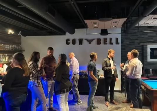 A group of people are standing around a pool table in a bar.