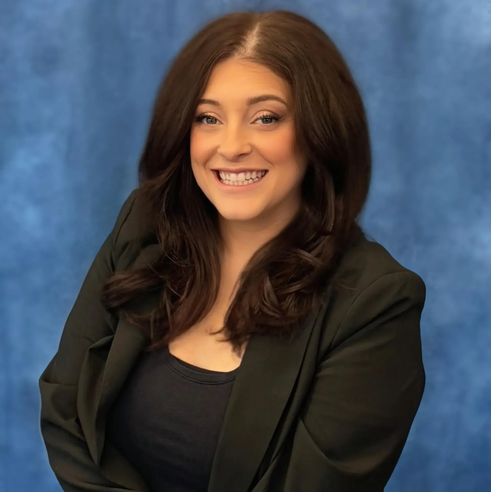 Smiling woman in a black blazer against a blue studio backdrop