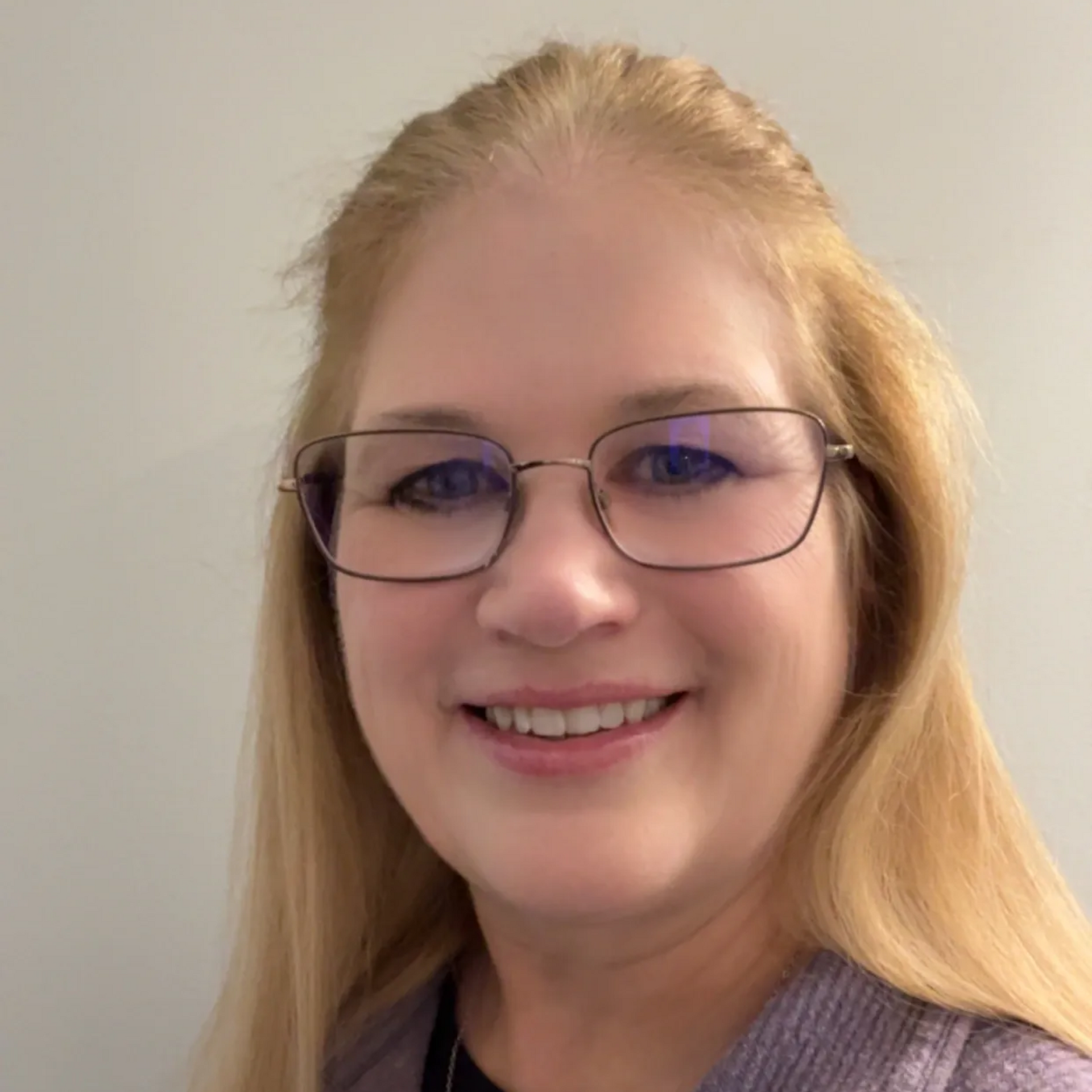 Woman with blonde hair and glasses smiles at the camera, wearing a purple sweater.