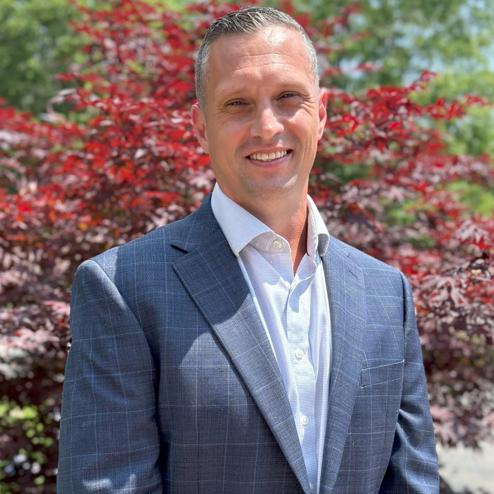 A woman in a black suit is standing in front of a gray wall.