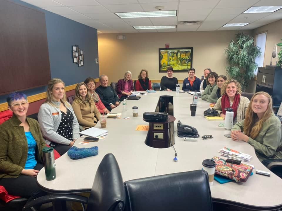 A group of people are sitting around a long table in a conference room.