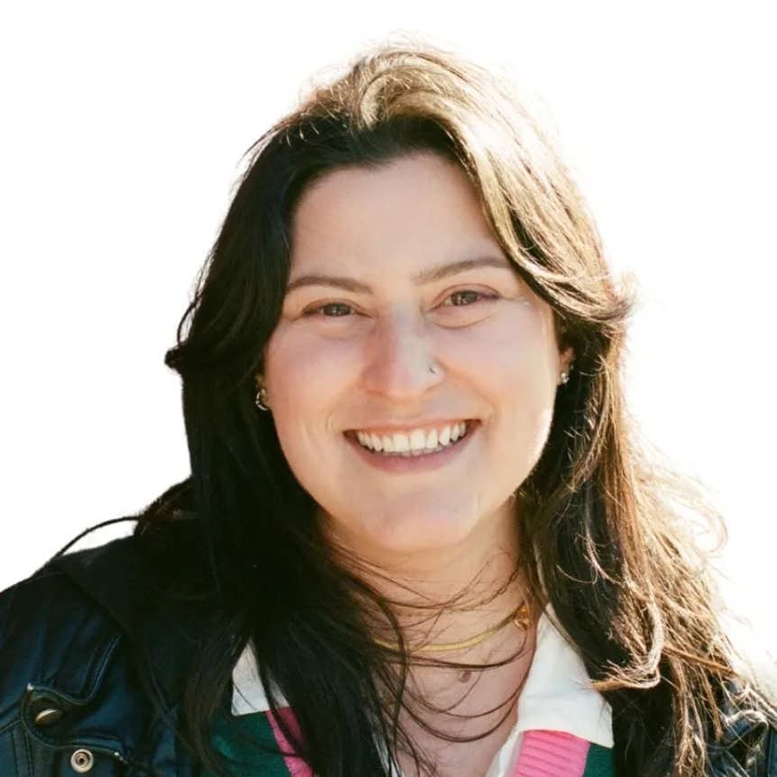 Woman with blonde hair and glasses wearing a blue top, smiling at the camera, against a gray background.