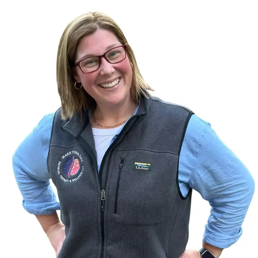 A smiling man in a green sweater poses outdoors with arms crossed, in front of a multi-story building.