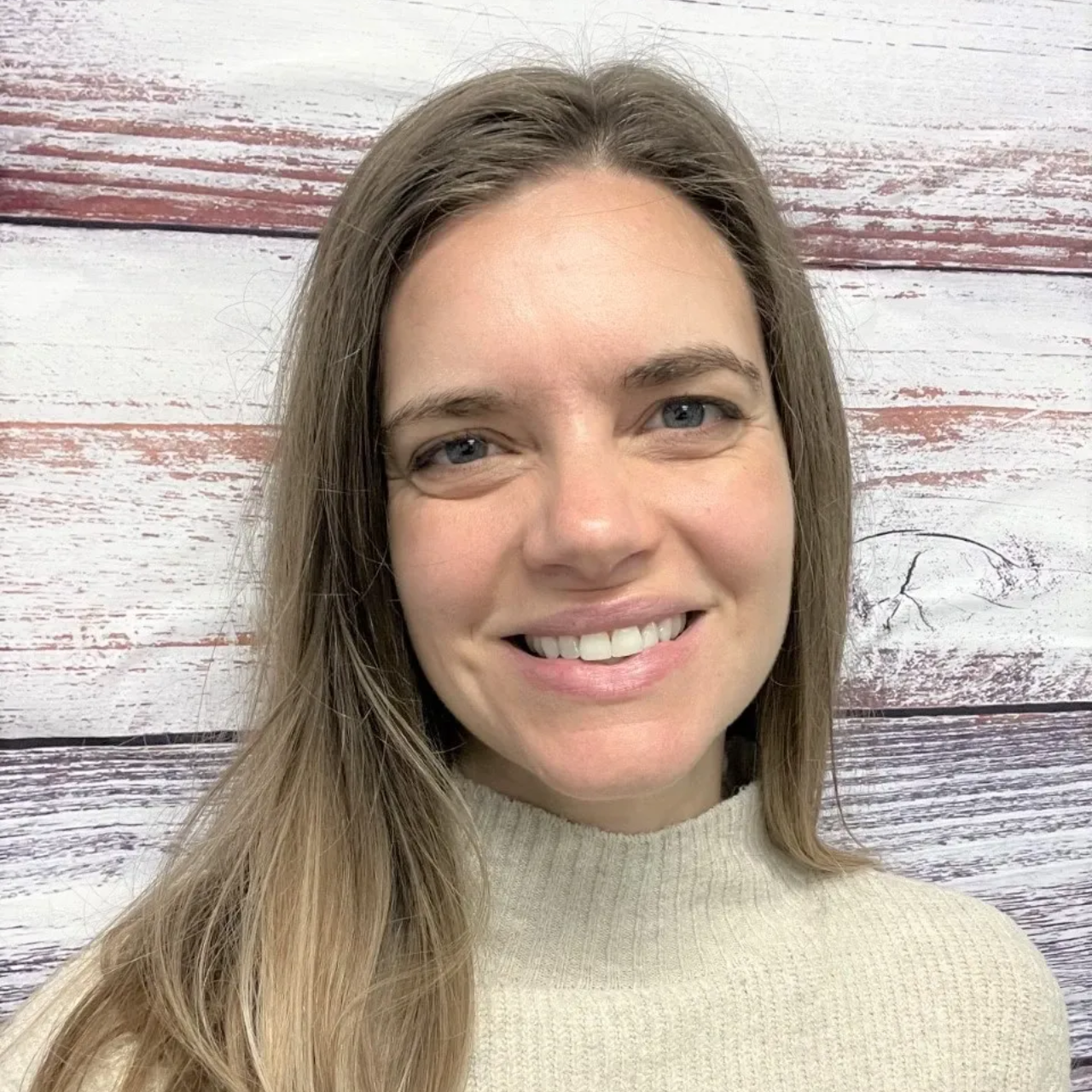 Smiling woman in a cream sweater against a whitewashed wood background