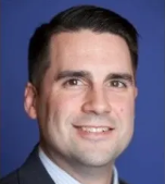 Smiling man in a suit against a blue background.