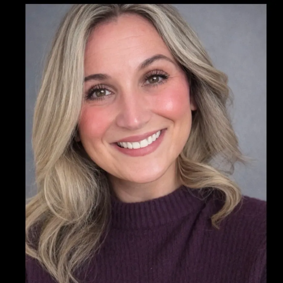 Woman with blonde hair smiles, wearing a purple sweater.