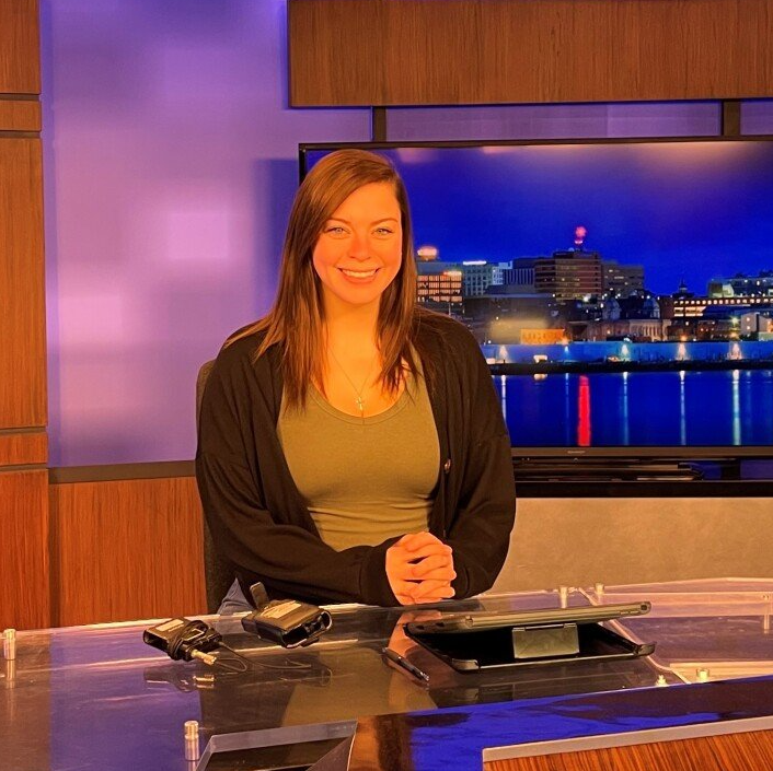 A woman is sitting at a desk in front of a television