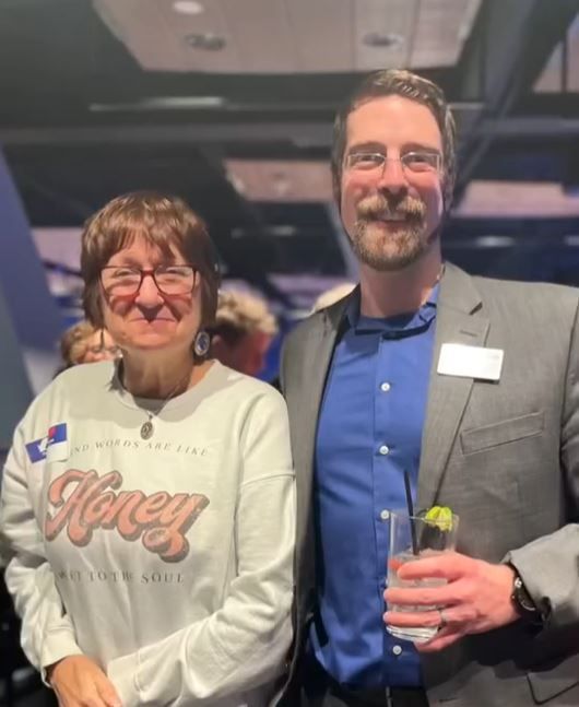 A man and a woman are posing for a picture and the woman is wearing a honey shirt
