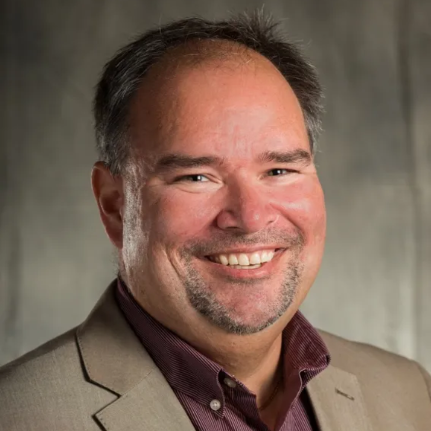 A young man with a beard is wearing a black shirt and smiling at the camera.
