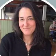 Man with short, curly gray hair, wearing a navy blue jacket, looking at the camera indoors.