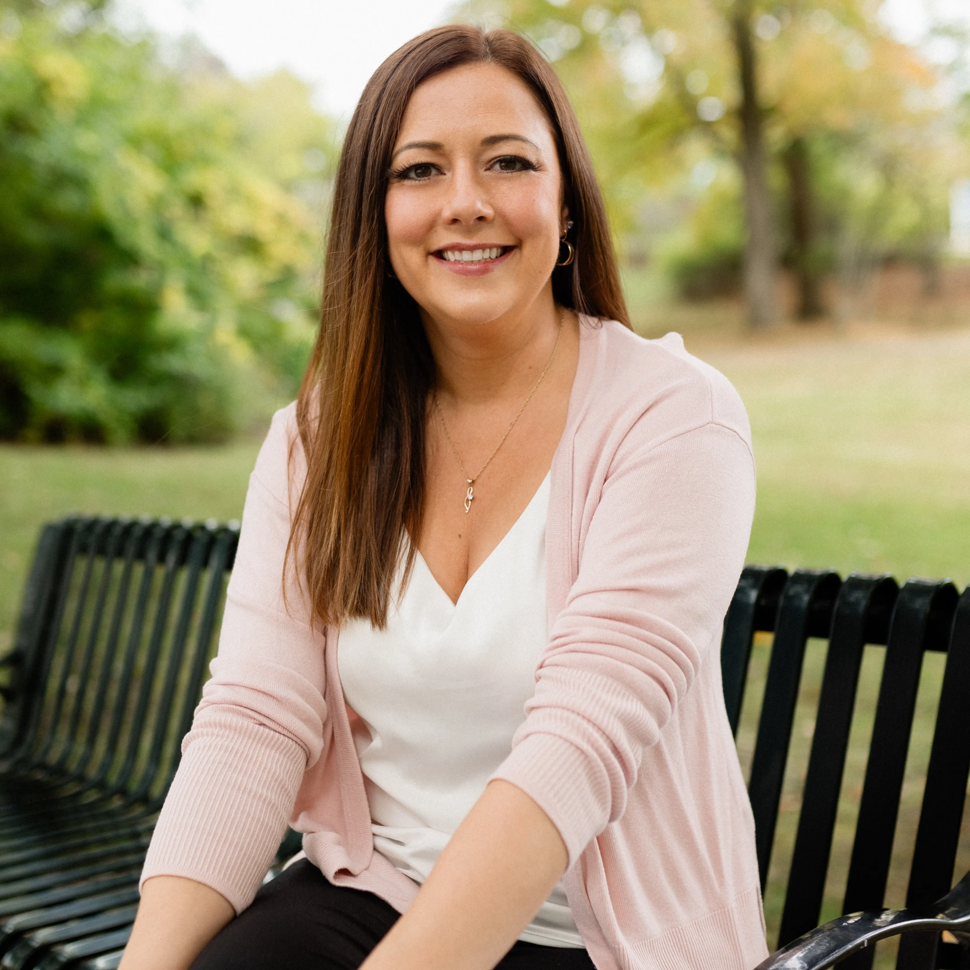 Woman in pink cardigan sitting on park bench, smiling.