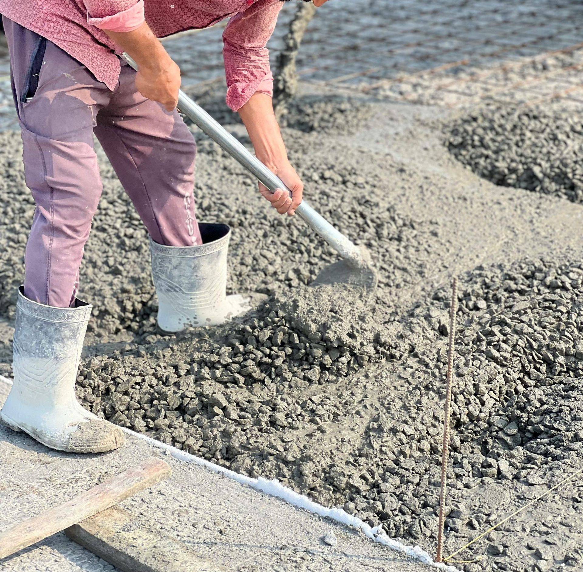 A man is pouring concrete with a shovel on a construction site.