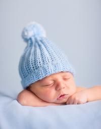 Newborn baby sleeping, wearing a light blue knit hat with a pom-pom.