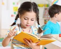 Girl with braids points to a page in an open yellow book, focused in a classroom setting.