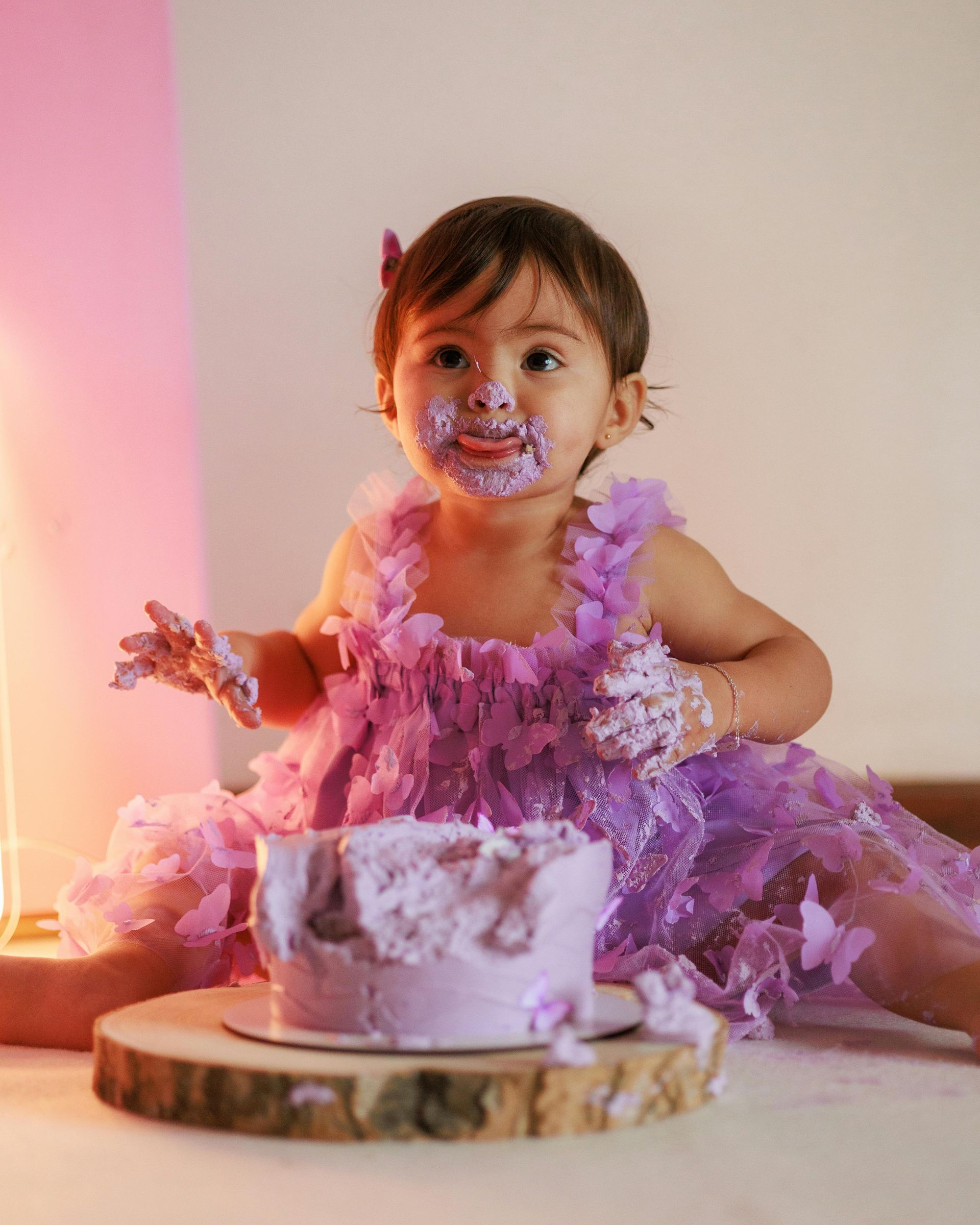 Child covered in purple frosting, sitting in front of a cake.