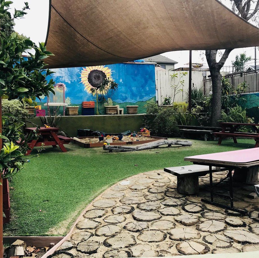 Outdoor play area with turf and wooden path; a painted sunflower on blue wall.