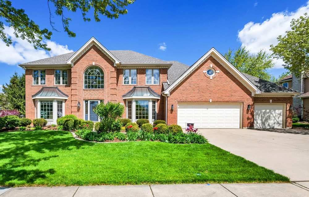 A large brick house with two garages and a lush green lawn.
