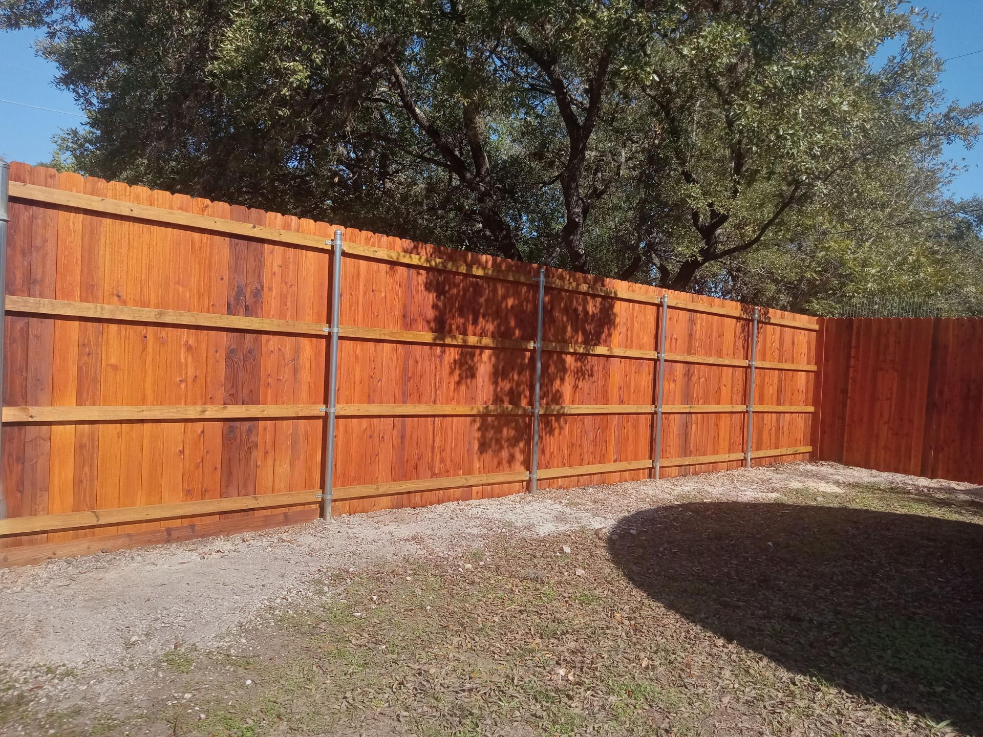A close up of a white picket fence with the sun shining through the trees in the background.