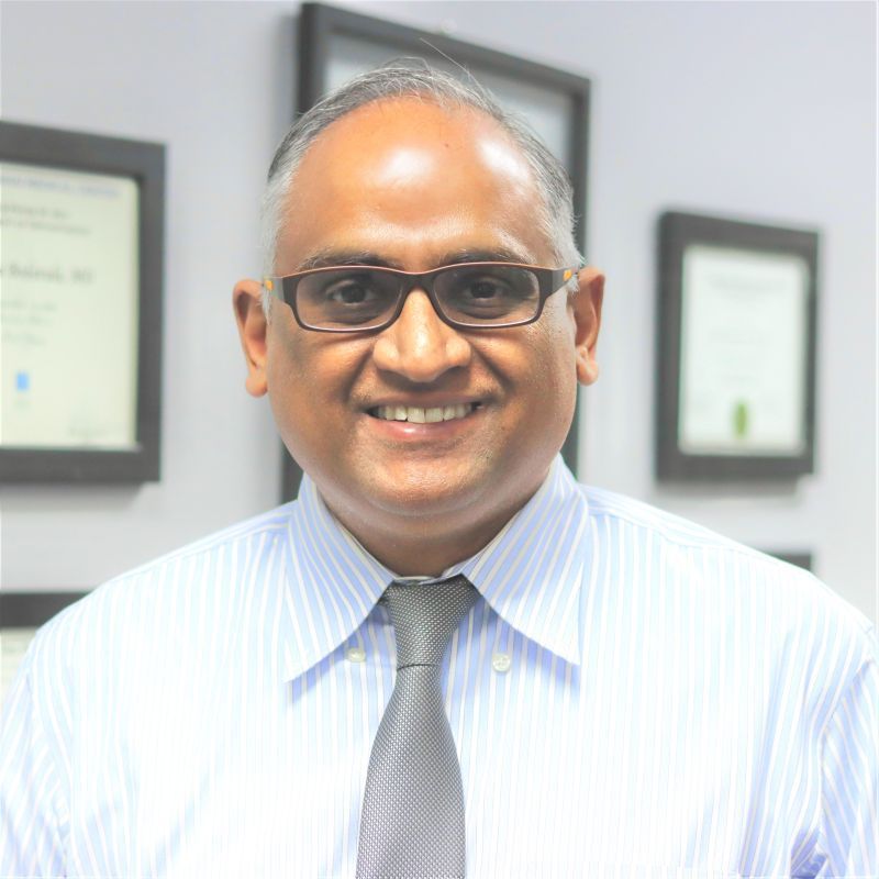 A man wearing glasses and a tie is smiling for the camera.