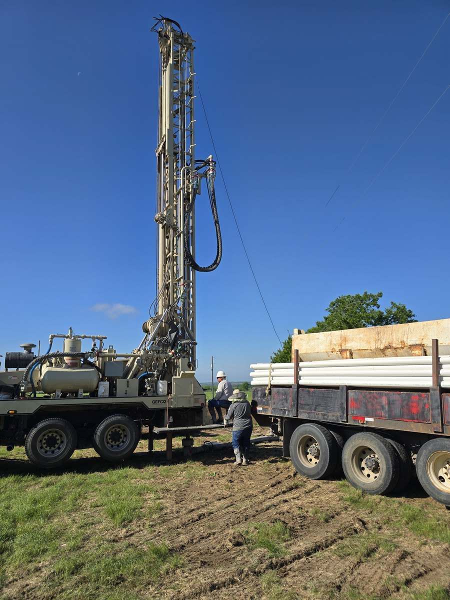 A water well contractor stands beside a truck with a drilling rig, part of a professional well service company setup.