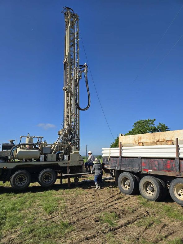 A water well contractor stands beside a truck with a drilling rig, part of a professional well service company setup.