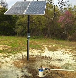A solar panel is sitting next to a water pump in a field.