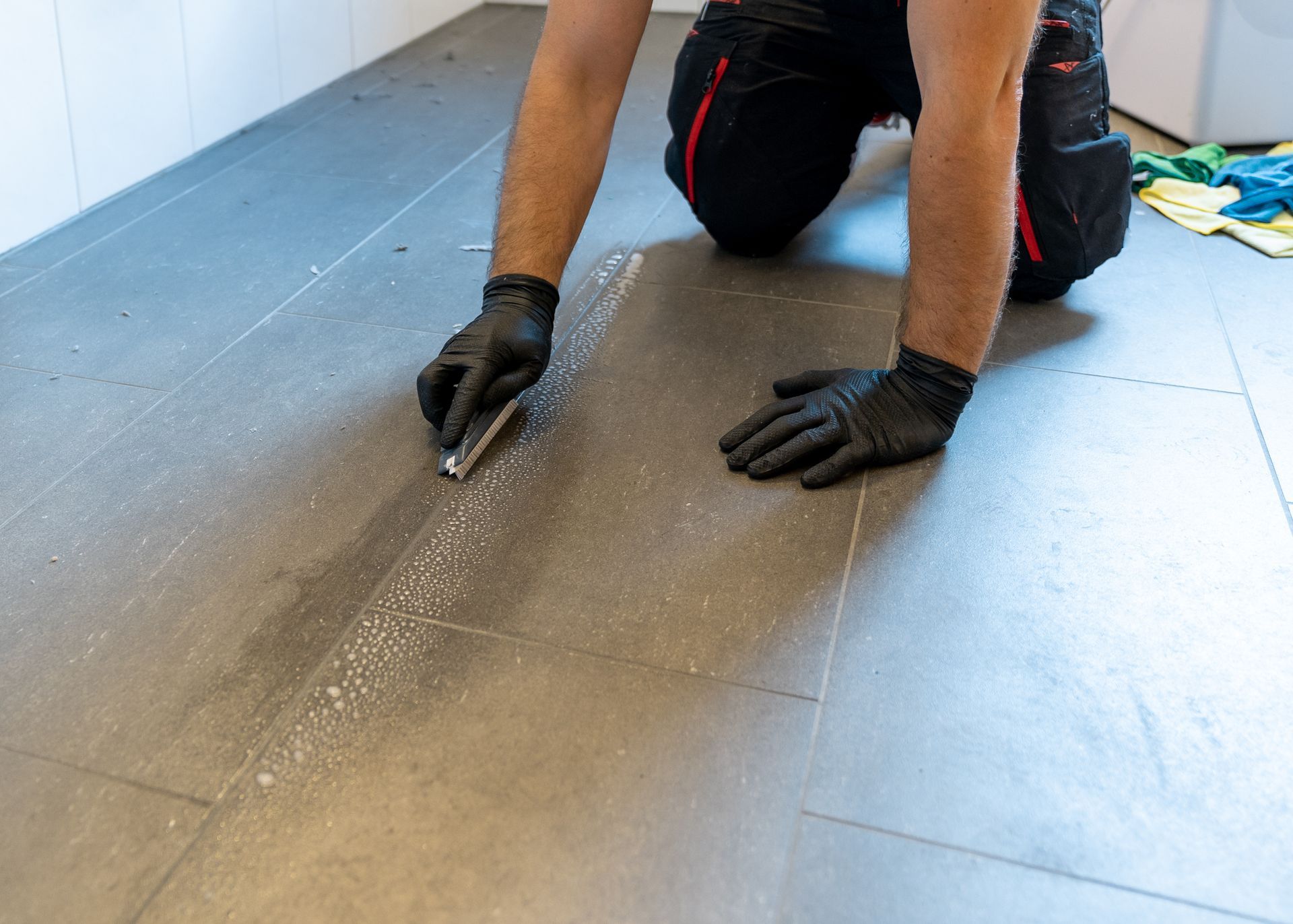 Technician scrubbing tile grout lines with a brush and cleaning solution.