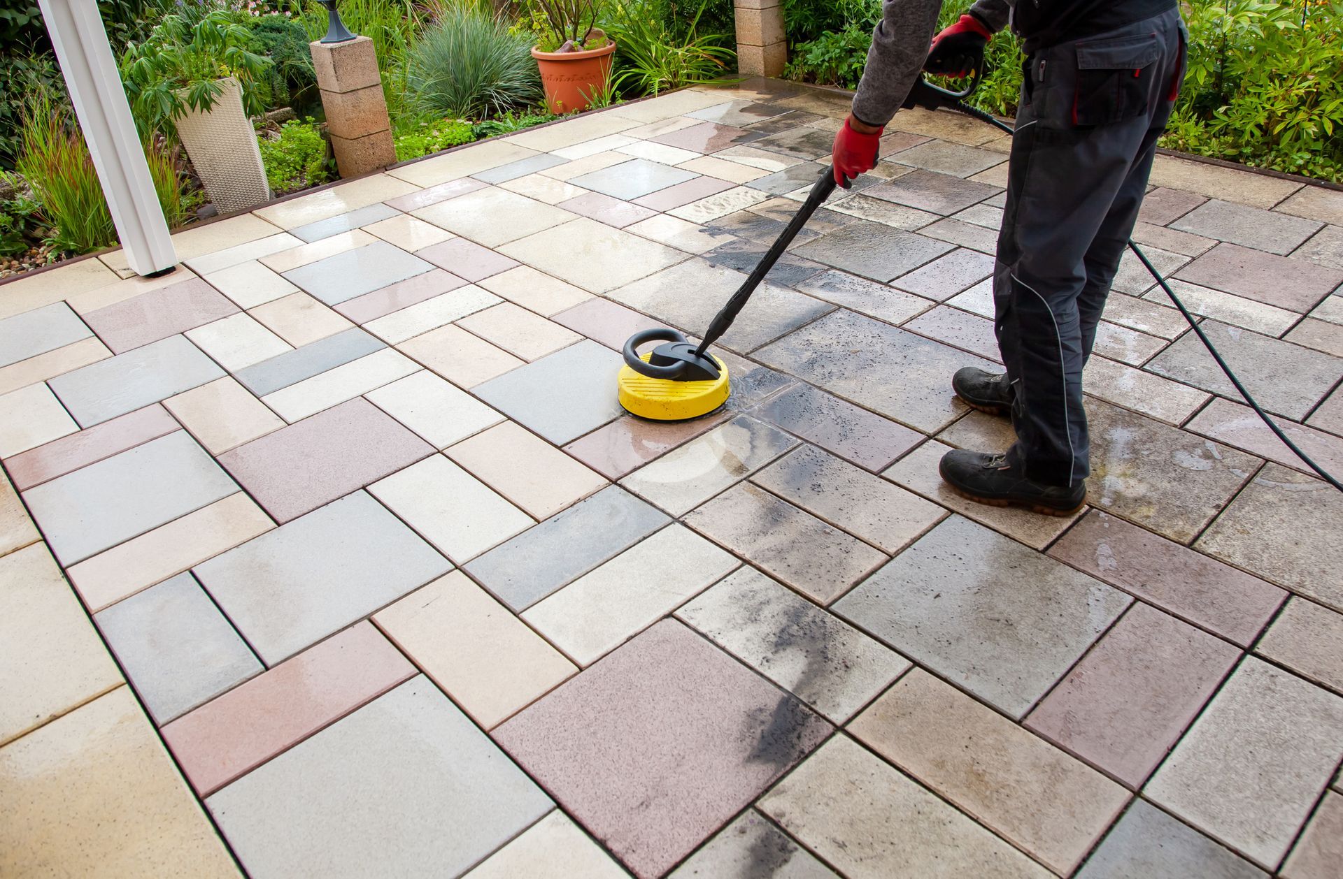 Tile and grout cleaning on patio performed by male worker with the high-pressure cleaner.