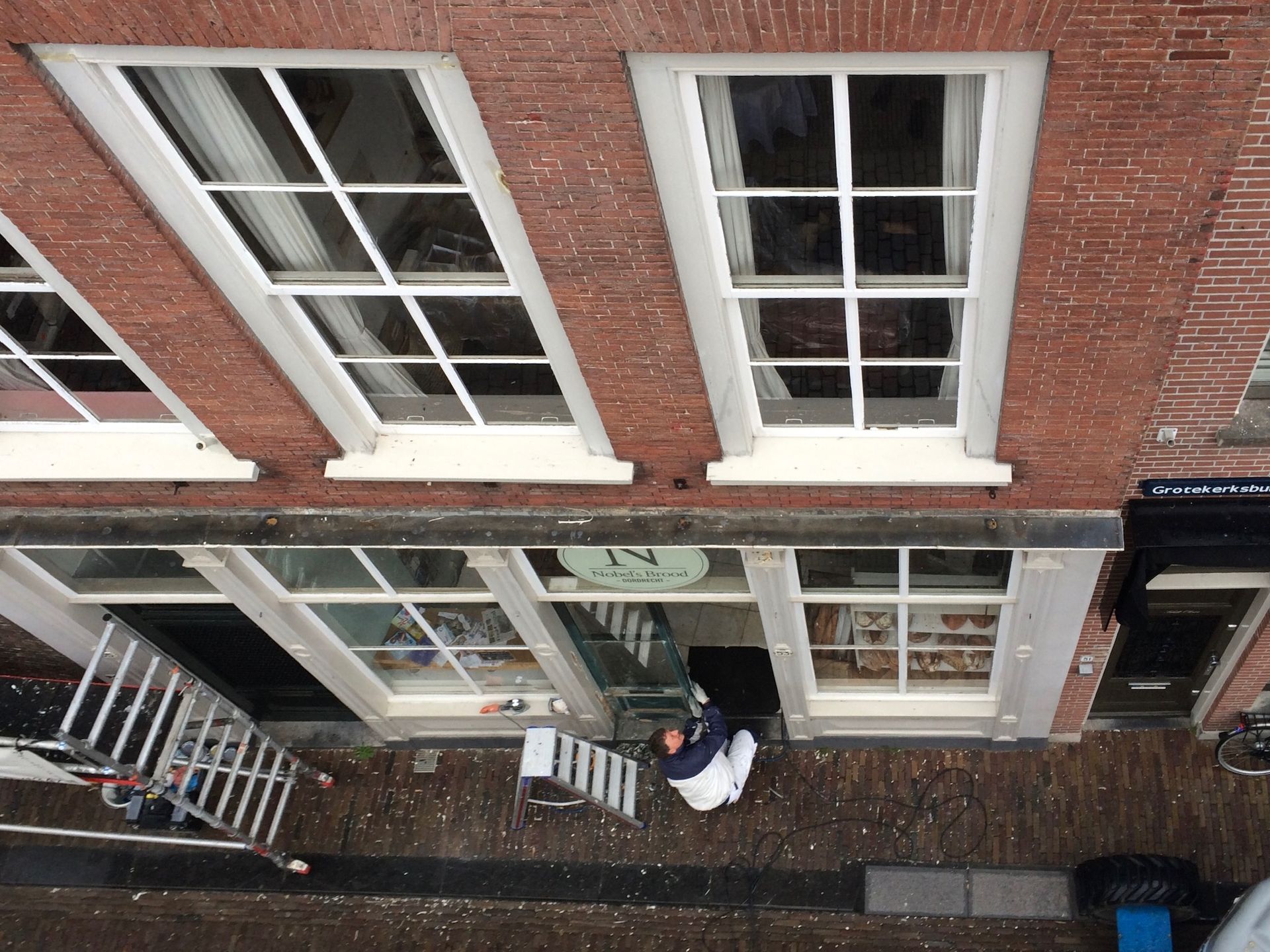 Bovenaanzicht van een bakstenen gebouw met witte ramen en een persoon in een deuropening.