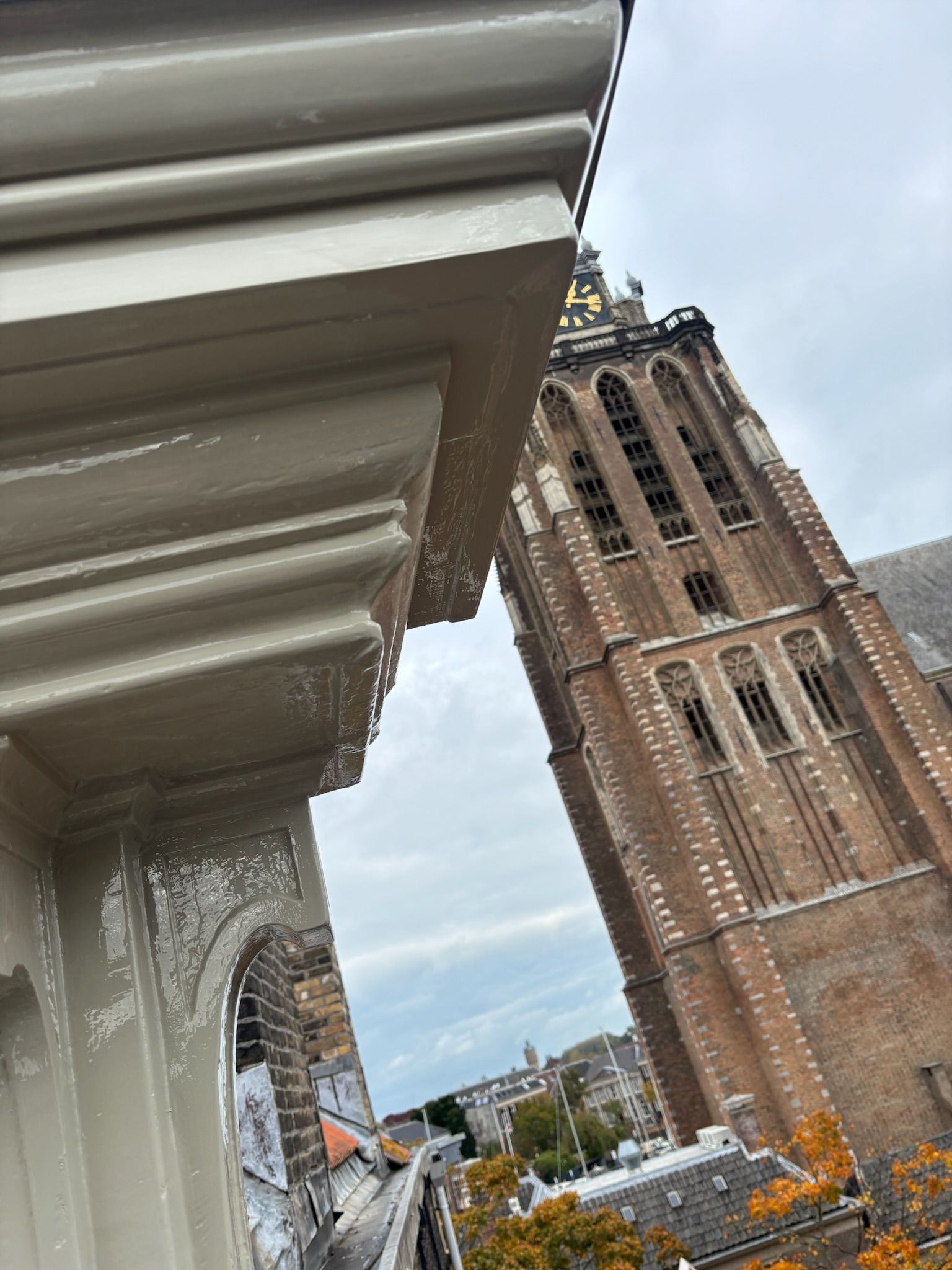 Close-up van een wit gebouw op de hoek, met een hoge bakstenen kerktoren tegen de bewolkte lucht op de achtergrond.