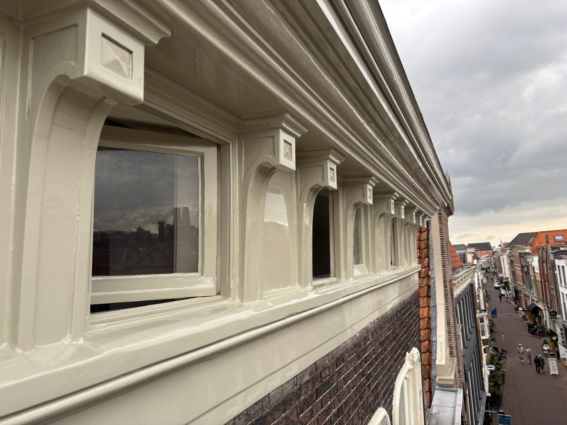 Beige geverfde gevel met meerdere ramen, gedetailleerde lijstwerken en een stadsgezicht op de achtergrond.