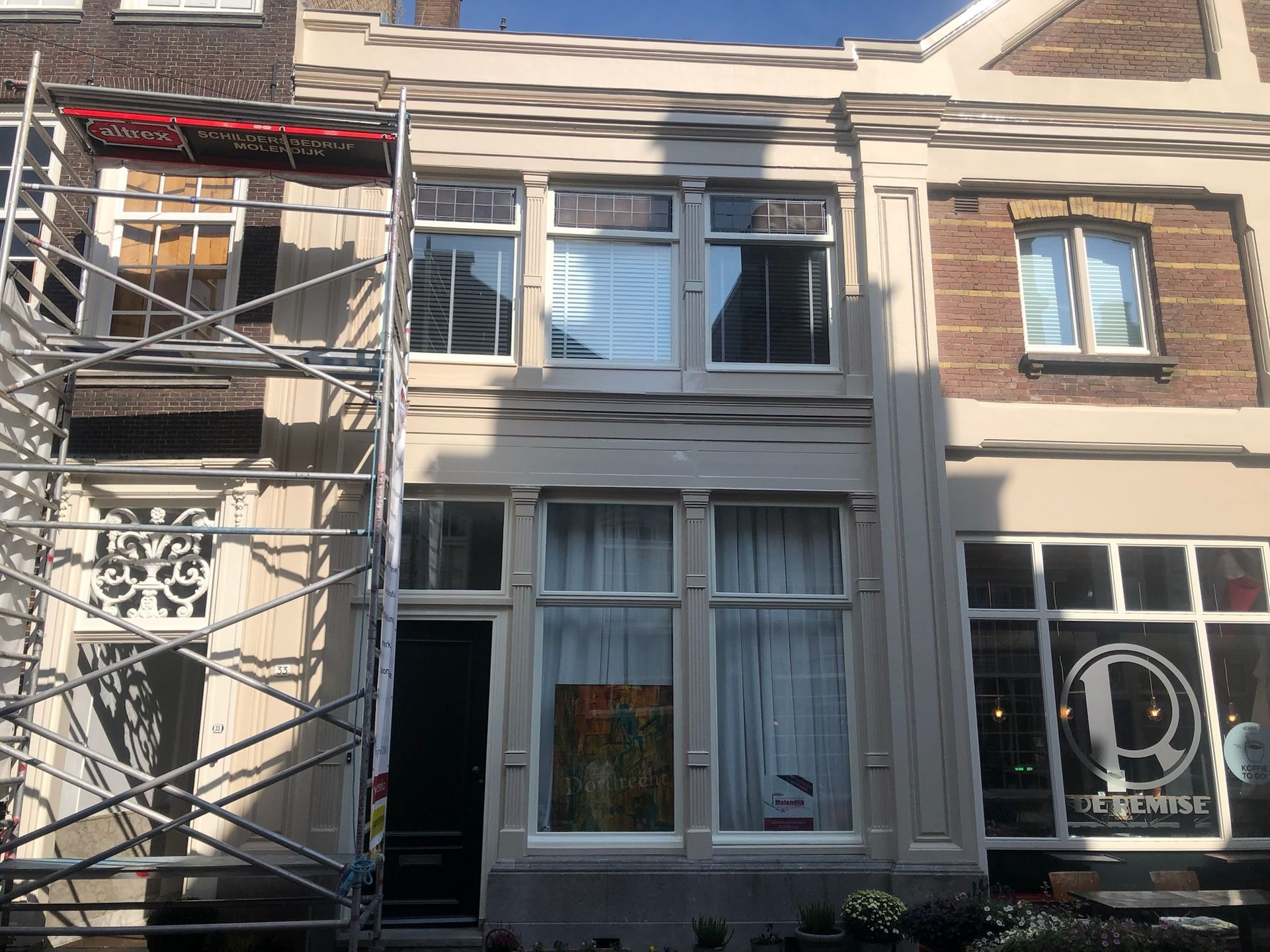 Gevel van een gebouw dat gerenoveerd wordt, steigers zichtbaar. Ramen en deur.