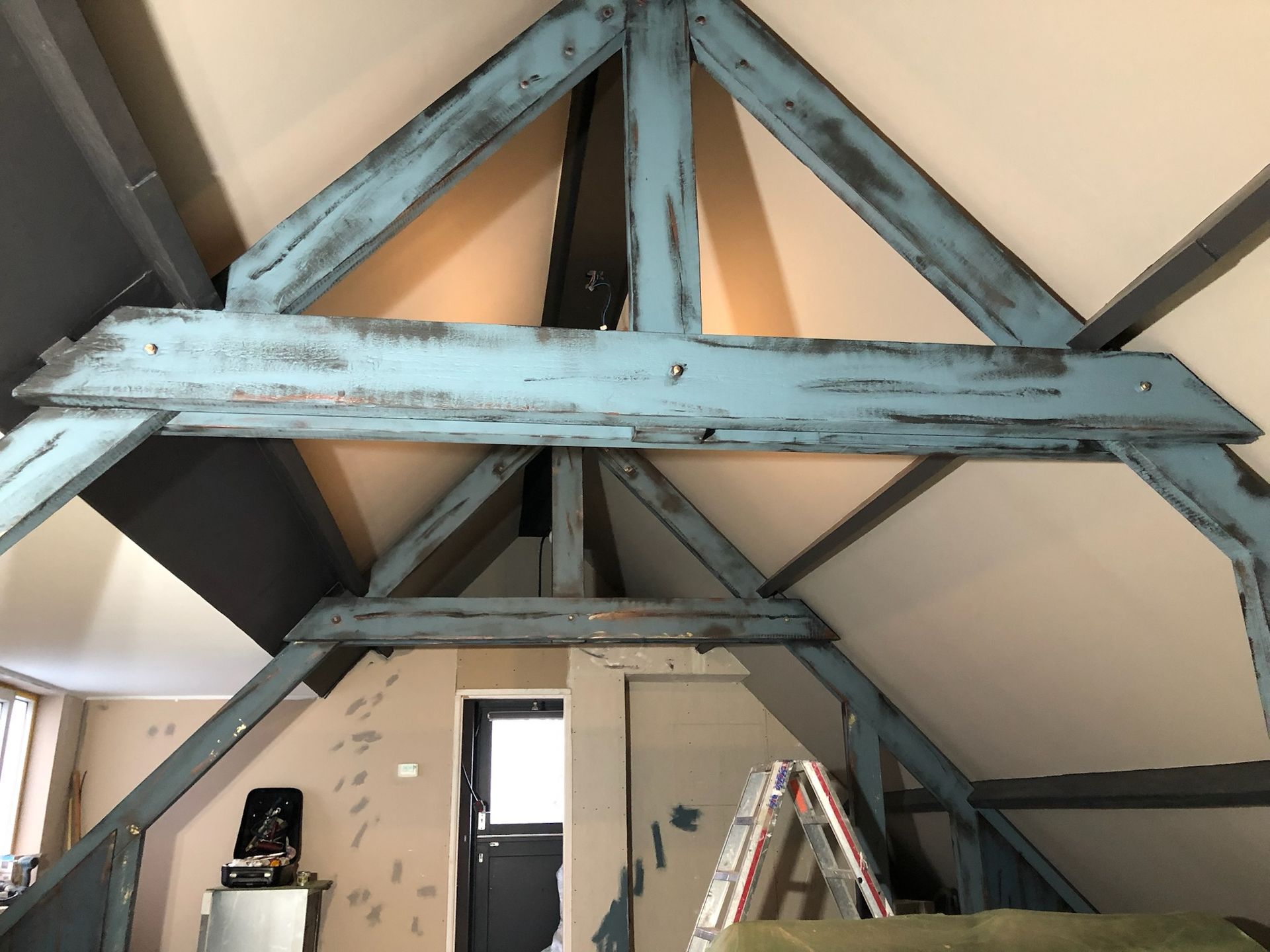 Blauw geverfde houten balken op zolder, die het dak ondersteunen.