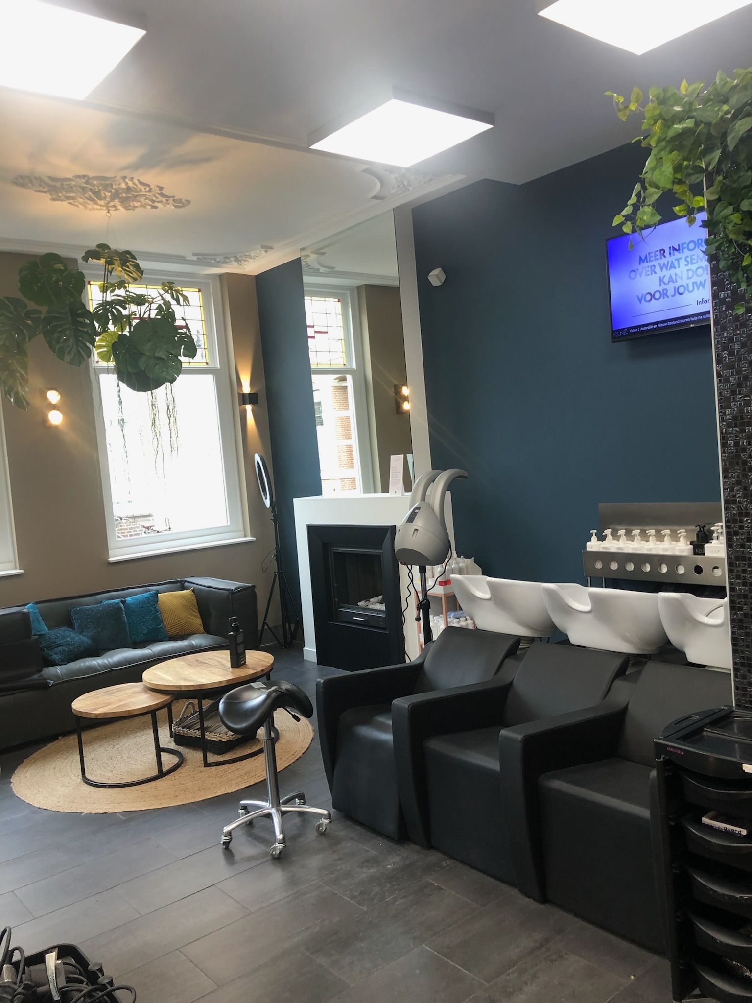 Interieur van een kapsalon met zitplaatsen, wasstations en decoratieve planten.