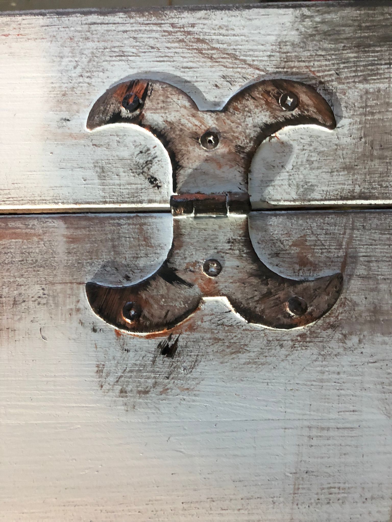 Close-up van een verweerd, decoratief metalen scharnier op een geverfd houten oppervlak, met tekenen van slijtage en roest.